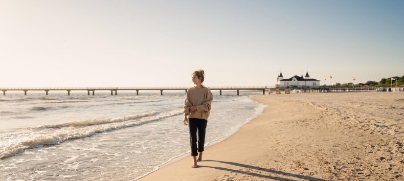 Frau spaziert am Strand von Ahlbeck zum Sonnenaufgang mit Seebrücke im Hintergrund