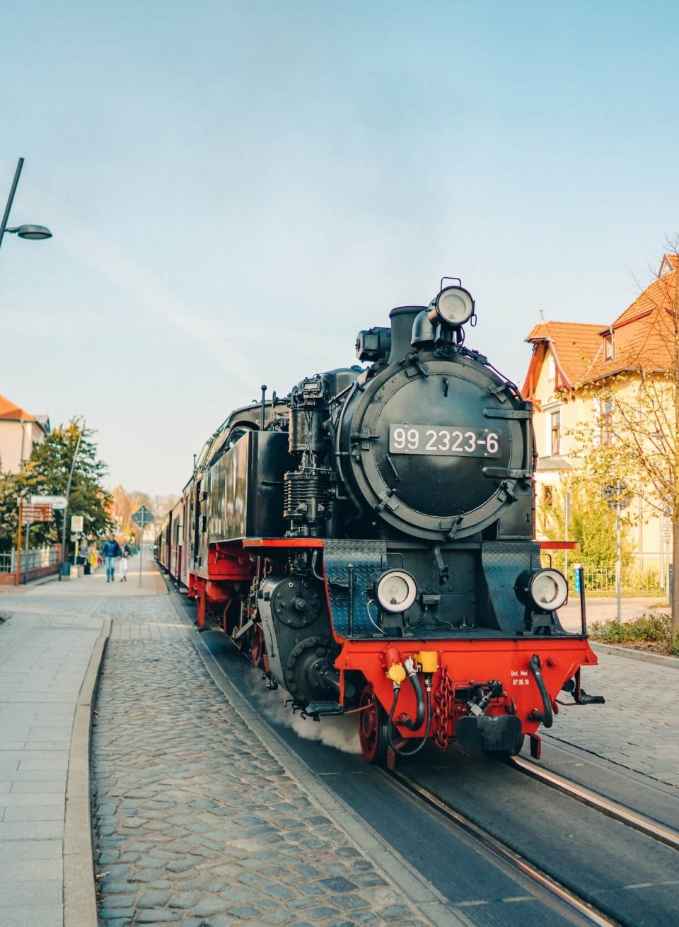 Die Mecklenburgische Bäderbahn “Molli” als Dampflok im Stadtzentrum von Bad Doberan, umgeben von Häusern und Spaziergängern.