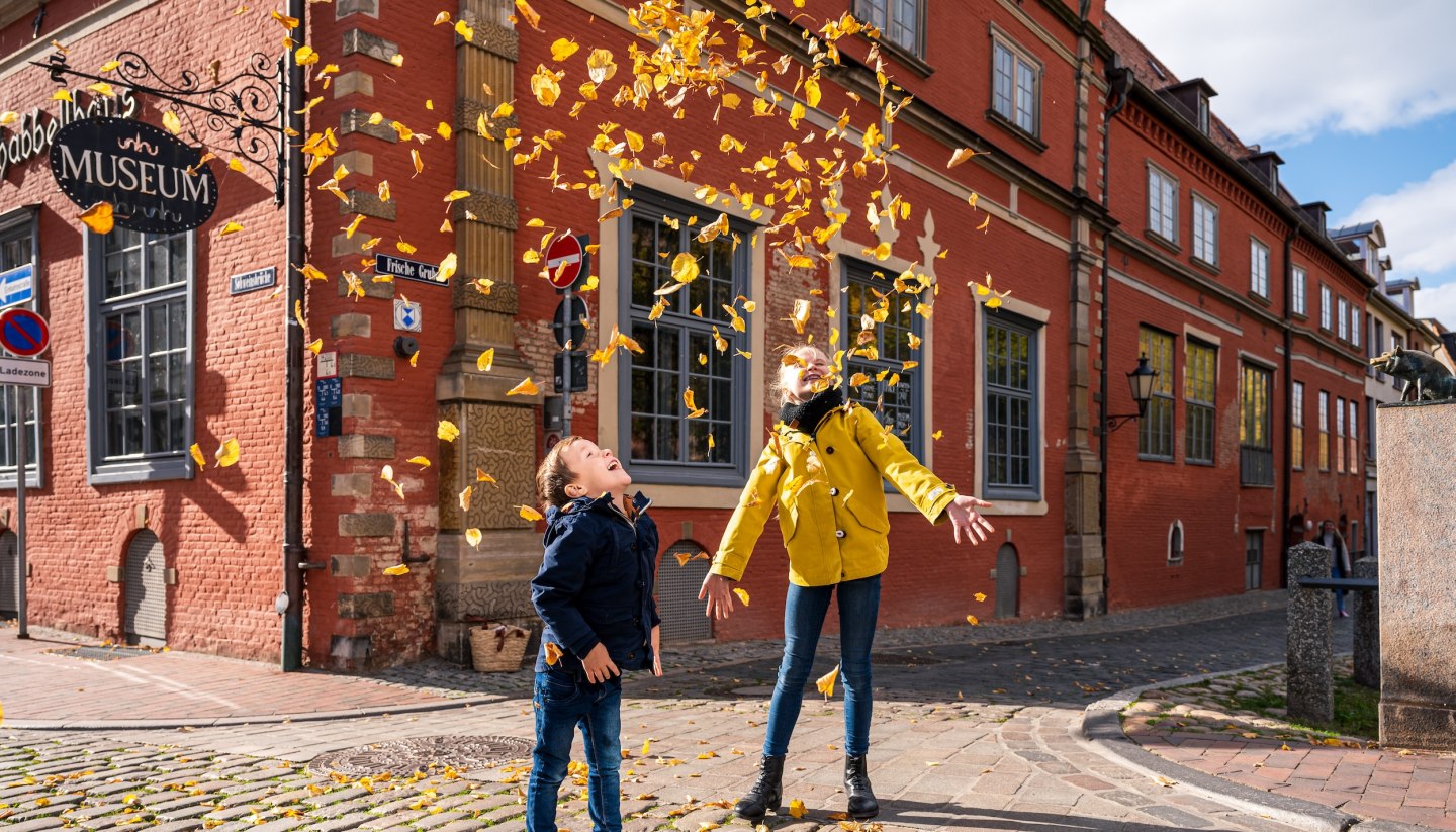 Herbstferien an der Mecklenburgischen Ostseeküste und Kinder spielen mit den Herbstblättern vor dem Schabbell Museum.