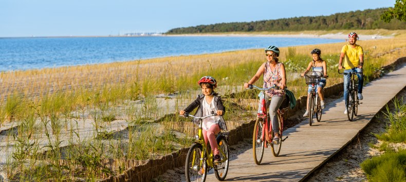 Eine vierköpfige Familie fährt mit dem Fahrrad auf dem Radweg am Strand entlang.