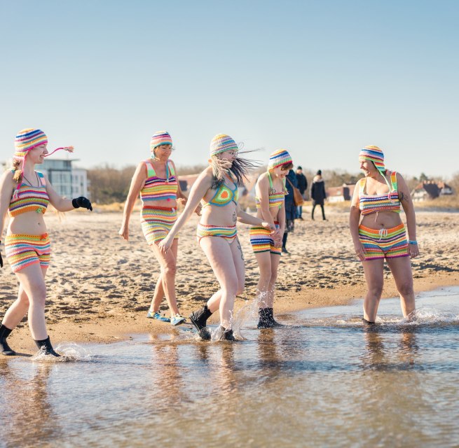 Eisbader gehen am Strand von Warnemünde in die Ostsee bei Sonnenschein.