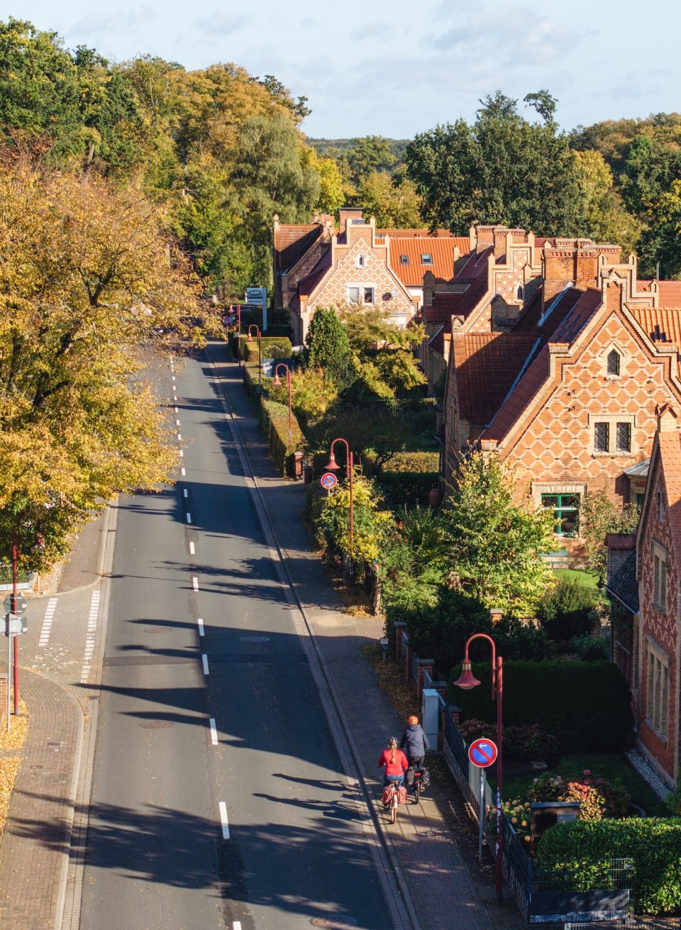 Luftaufnahme einer herbstlichen Straße in Raben-Steinfeld, gesäumt von Bäumen und historischen Häusern, mit Radfahrern im Vordergrund.