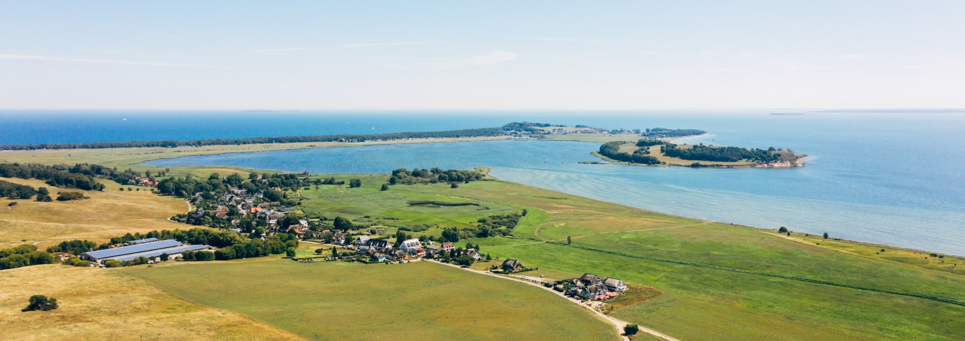 Luftaufnahme der Zicker Berge auf der Halbinsel Mönchgut mit weiten Wiesen, kleinen Dörfern und Blick auf die Ostsee und umliegende Halbinseln unter klarem Himmel.