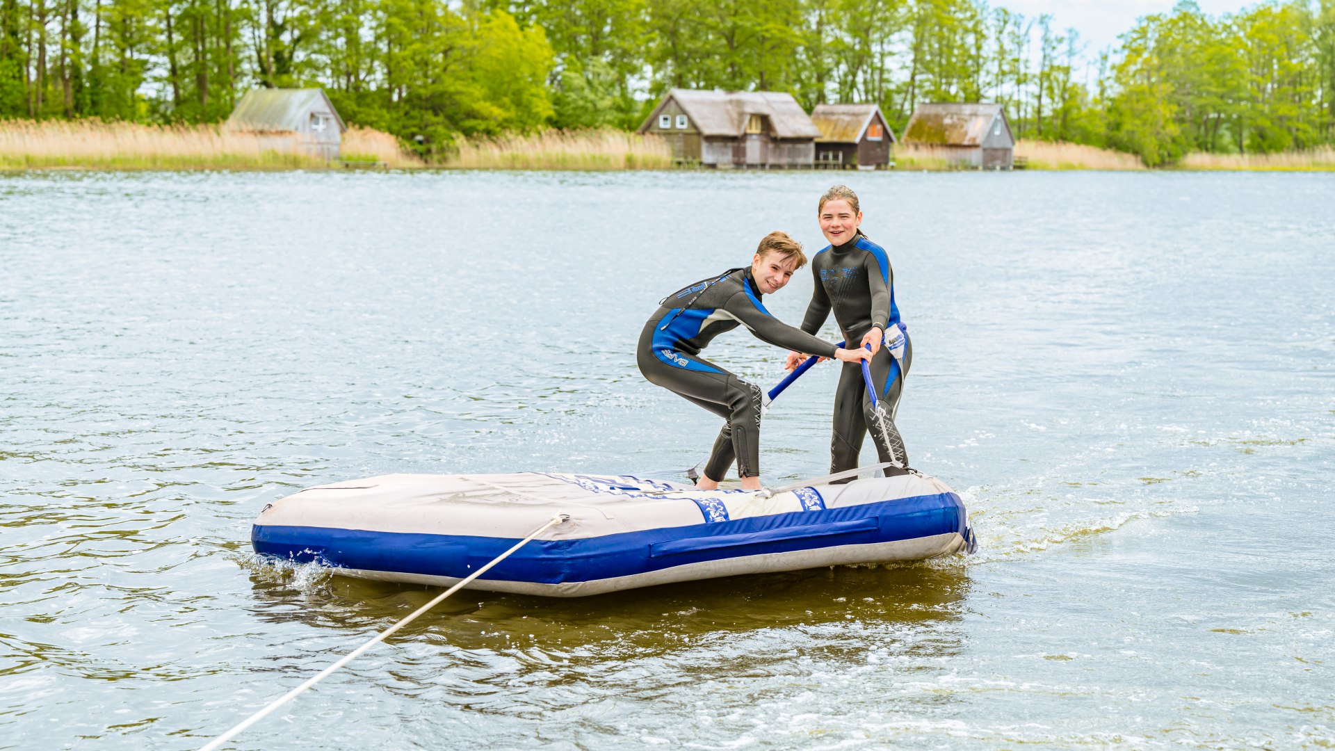 Auf der Badeinsel lassen sich Ferri und Theo über den See ziehen. Wer schafft es, länger stehen zu bleiben? , © TMV/Tiemann