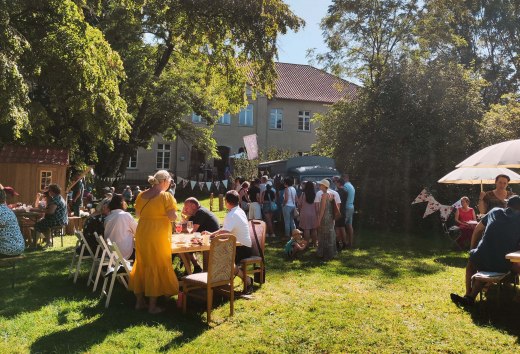 Die MitsommerRemise im Gutspark Klocksin mit Speisen und Getränken. Menschen sitzen an Tischen im Park hinter dem Gutshaus.