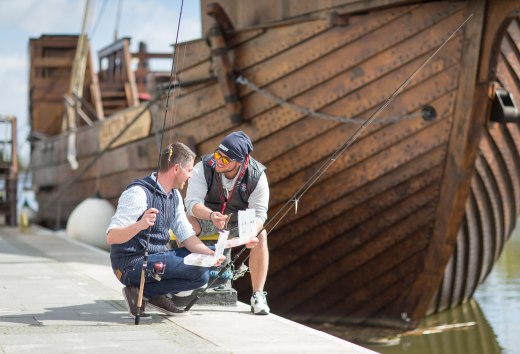 Junge Männer angeln am Stadthafen in Ueckermünde mit einer Kogge im Hintergrund., © TMV/Läufer