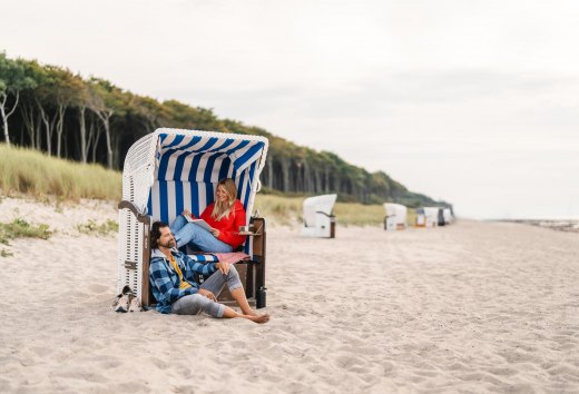 Pärchen sitzt in einem Strandkorb am Strand von Graal-Müritz an der Ostseeküste. Im Hintergrund ist der Küstenwald zu sehen.