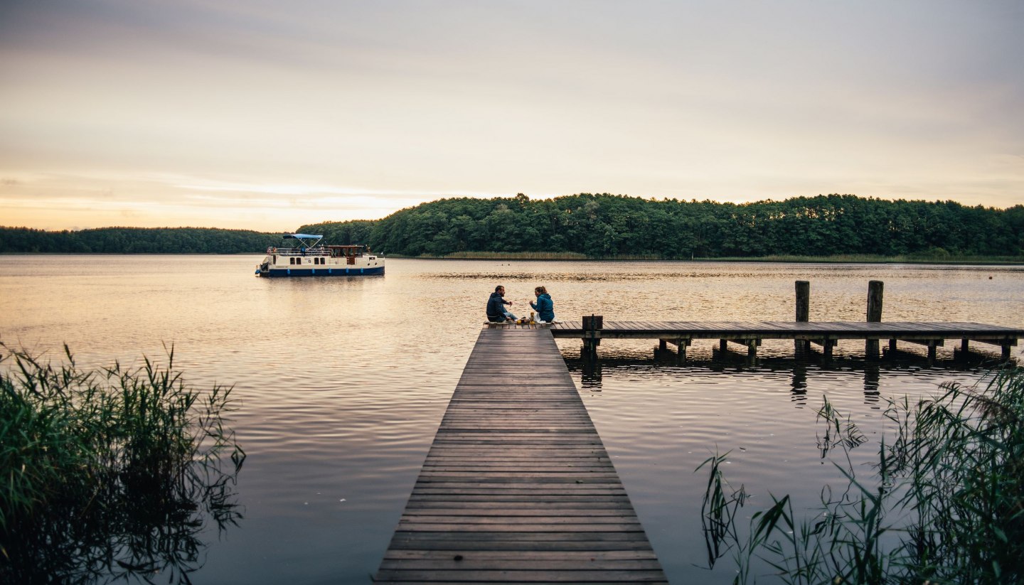 Ein entspanntes Picknick auf einem hölzernen Steg: Umgeben von friedlicher Natur genießen Menschen die ruhige Atmosphäre am Wasser.