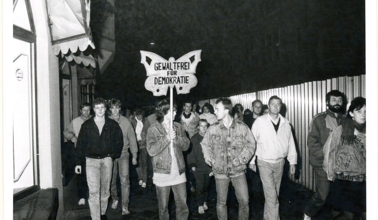 Demonstrierende führen ein Transparent in Form eines Schmetterlings mit sich, auf dem steht "Gewaltfrei für Demokratie", © Bundesarchiv/Stasi-Unterlagen-Archiv