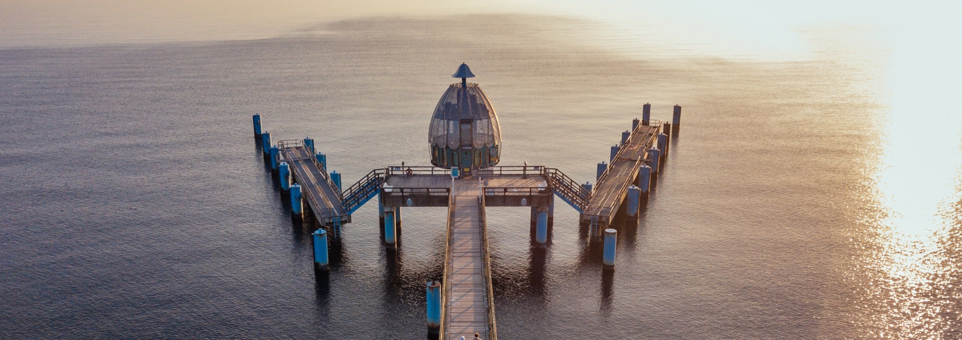 Drohnenaufnahme der Tauchgondel an der Seebrücke Sellin, mit Holzsteg und der Ostsee im goldenen Licht eines Sonnenuntergangs.