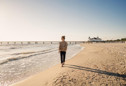 Frau spaziert am Strand von Ahlbeck zum Sonnenaufgang mit Seebrücke im Hintergrund