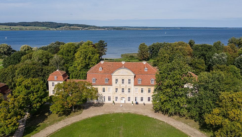 Luftaufnahmen von Schloss Kumerow, im Hintergrund glitzert der blaue See, © Tourismusverband Mecklenburgische Seenplatte/Tobias Kramer