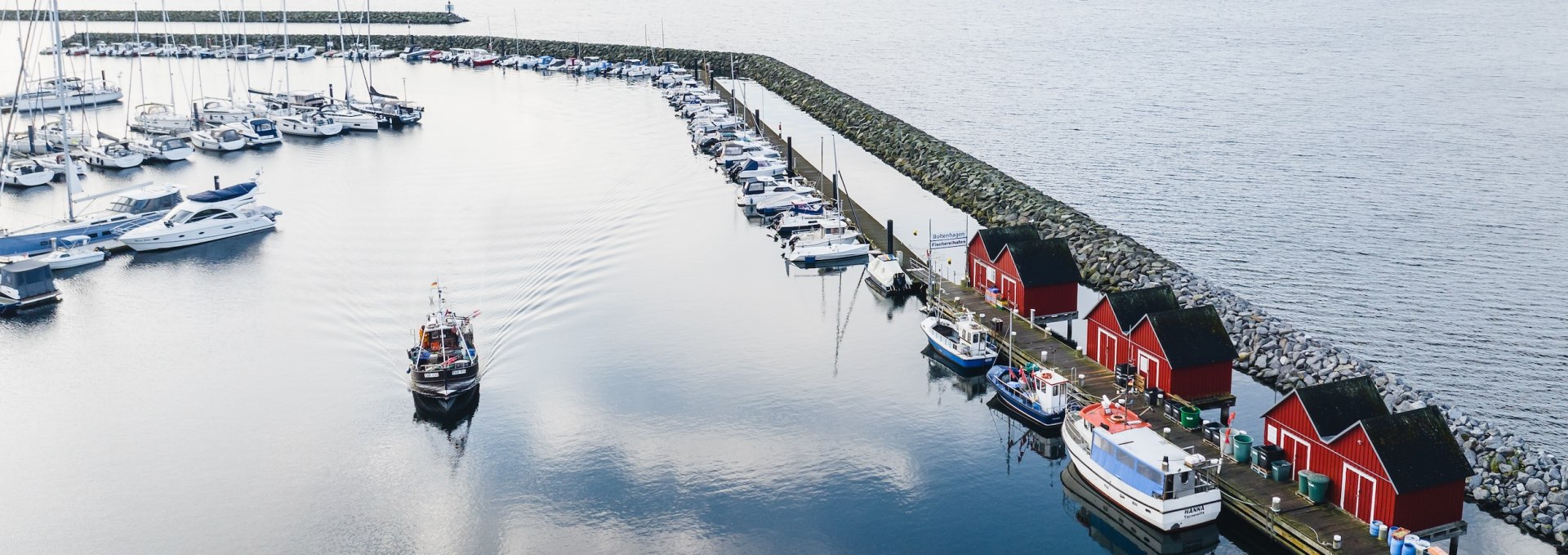 Bei der Ausfahrt aus dem Fischereihafen Boltenhagen passiert man die ikonischen roten Fischerschuppen, die sich hübsch in dem glatten Wasser des Hafenbeckens spiegeln., © TMV/Gross