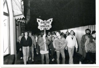 Demonstrierende führen ein Transparent in Form eines Schmetterlings mit sich, auf dem steht "Gewaltfrei für Demokratie", © Bundesarchiv/Stasi-Unterlagen-Archiv