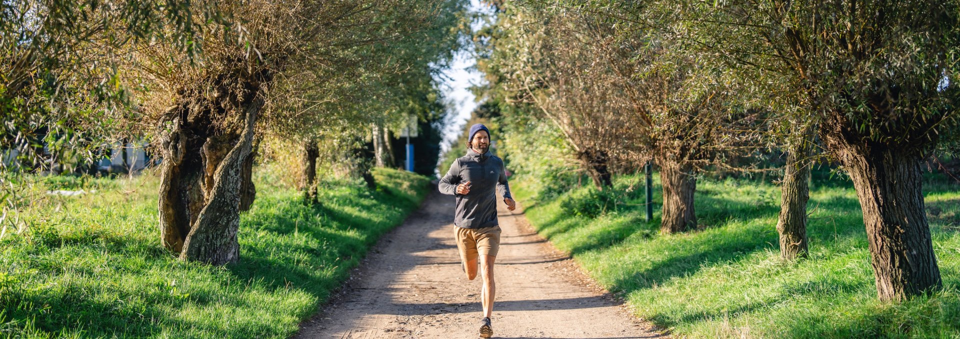  Ein Mann joggt auf einem von Bäumen gesäumten Weg auf der Insel Poel, umgeben von grüner Landschaft und sonnigem Wetter.