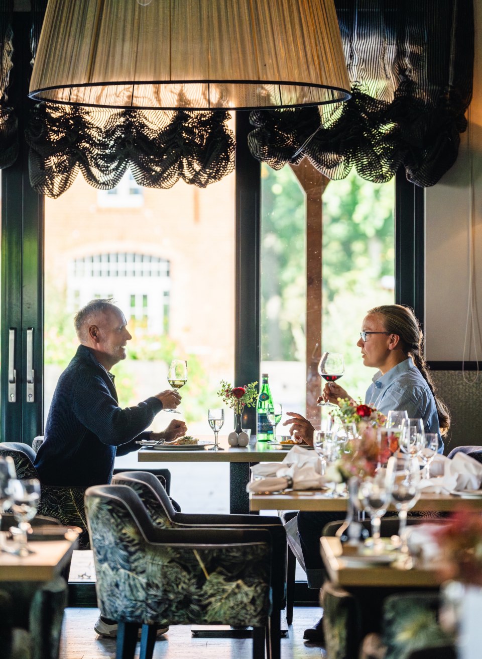 Zwei Personen stoßen mit einem Glas Wein an, während sie ein elegantes Mittagessen im Restaurant vom Schloss Basthorst genießen.