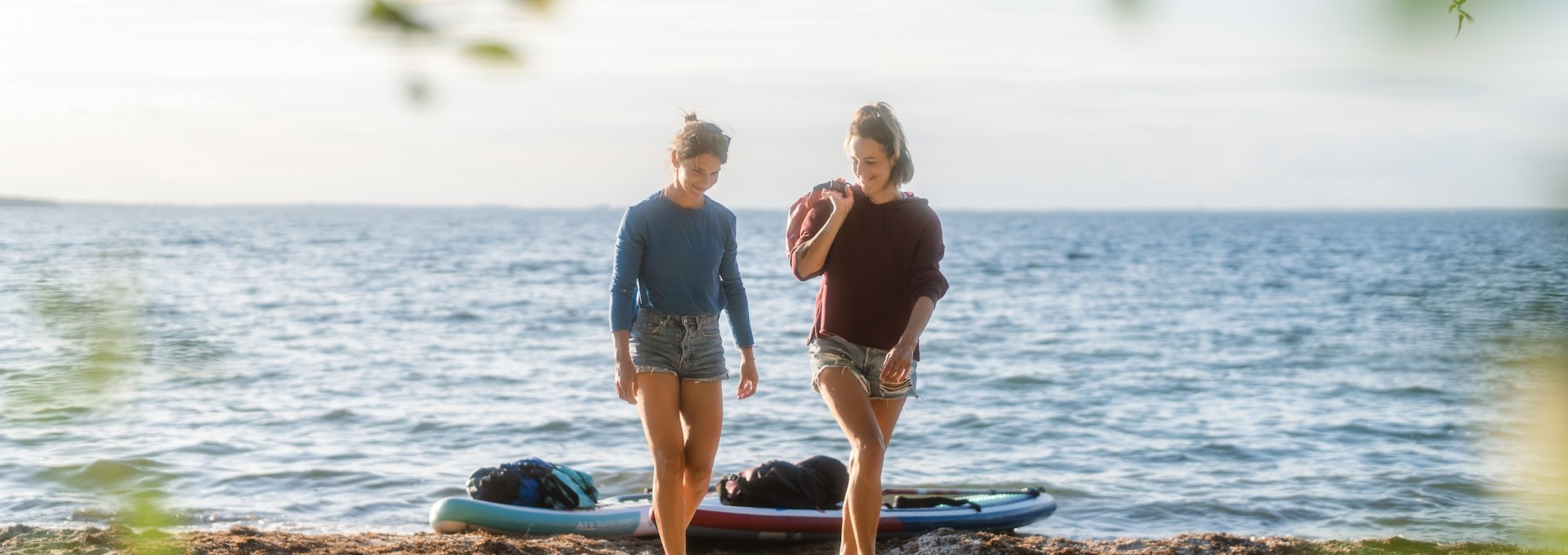 Die Sonne steht schon tief, als die beiden Freundinnen am kleinen Sandstrand vor dem Campingplatz Bolter Ufer die Boards an Land ziehen. Hinter ihnen wirkt die Müritz fast wie das Meer., © TMV/Gross