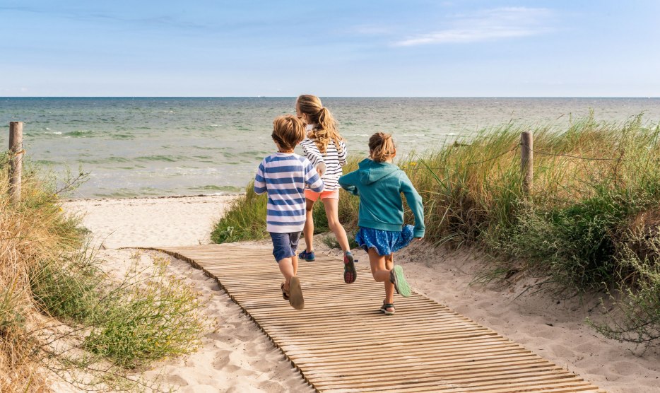 Kinder laufen fröhlich über den Holzsteg zum Strand an der Ostsee in Warnemünde, Mecklenburg-Vorpommern., © TMV/Süß