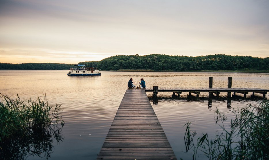 Ein entspanntes Picknick auf einem hölzernen Steg: Umgeben von friedlicher Natur genießen Menschen die ruhige Atmosphäre am Wasser.