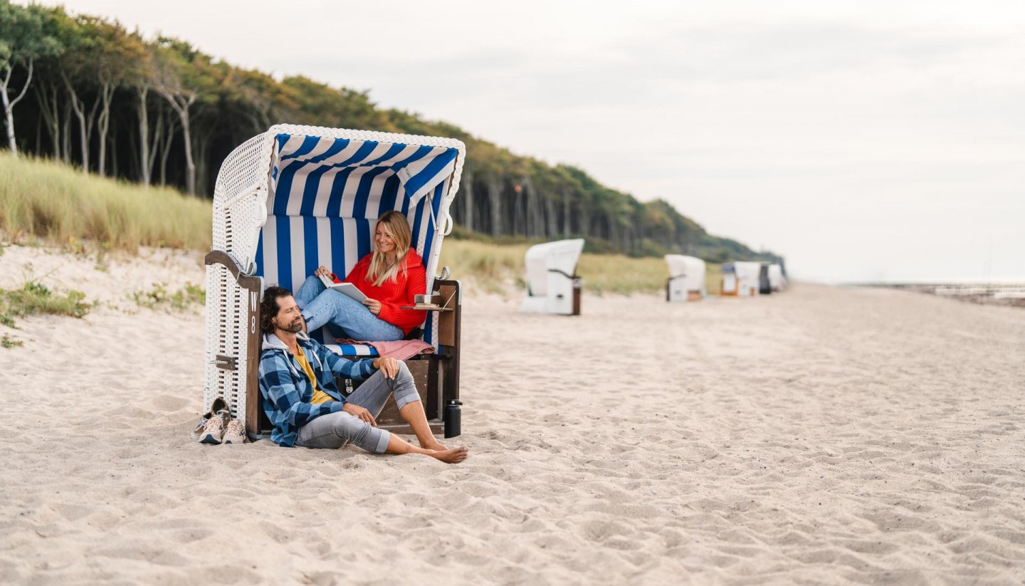 Pärchen sitzt in einem Strandkorb am Strand von Graal-Müritz an der Ostseeküste. Im Hintergrund ist der Küstenwald zu sehen.