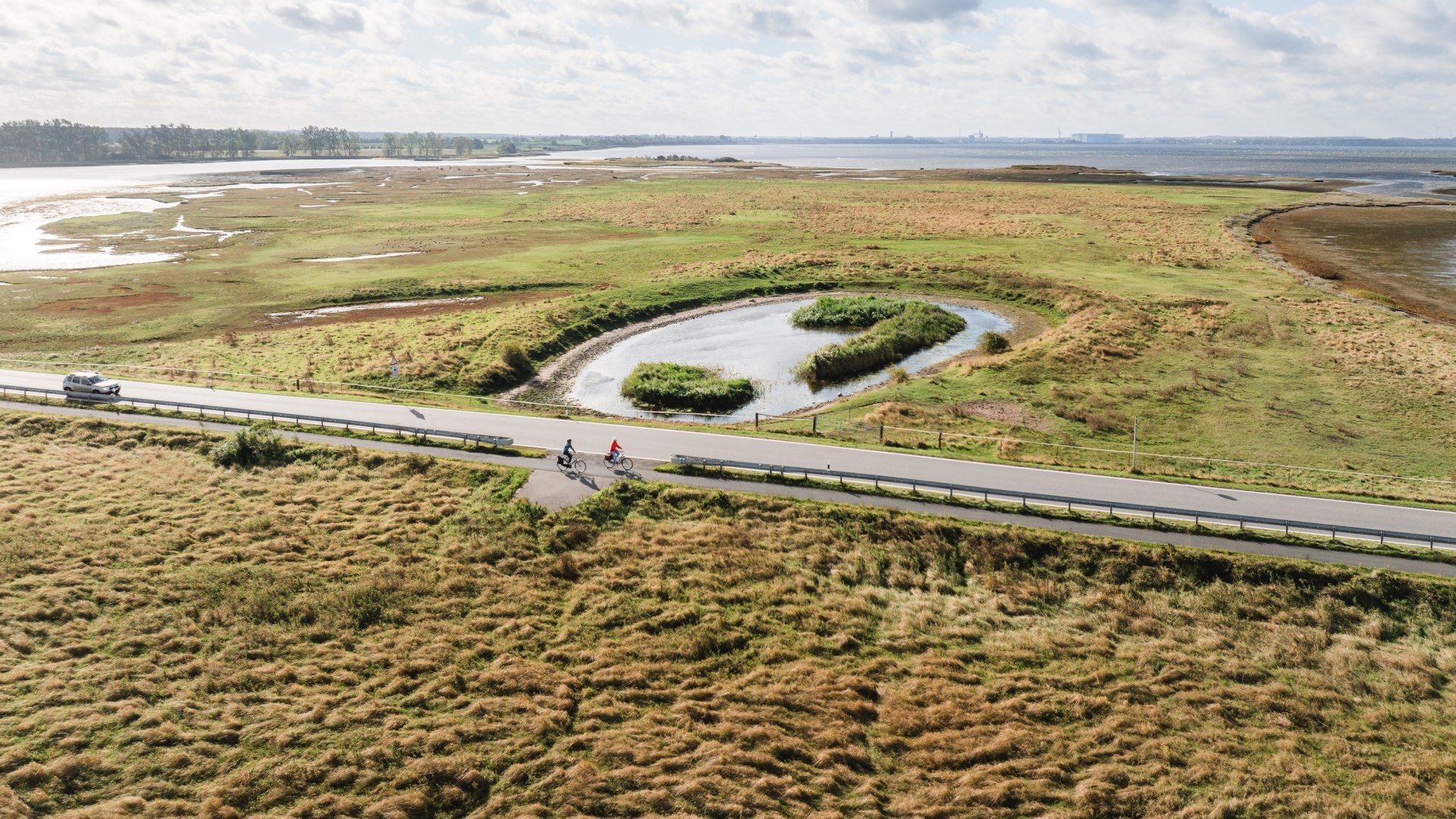  Luftaufnahme von Radfahrern auf einer Straße, die durch die grüne Küstenlandschaft der Insel Poel führt.