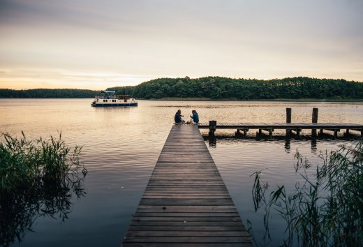 Ein entspanntes Picknick auf einem hölzernen Steg: Umgeben von friedlicher Natur genießen Menschen die ruhige Atmosphäre am Wasser.