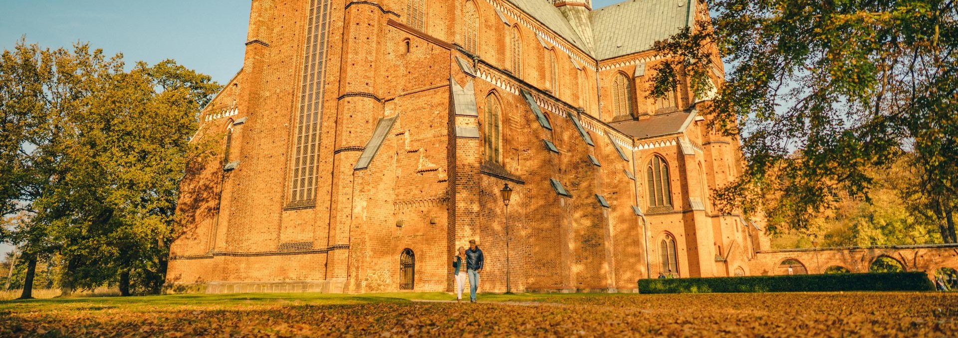 Ein Paar wandert im Herbst vor dem Münster Bad Doberan. Laub liegt vor dem Kloster auf dem Boden.