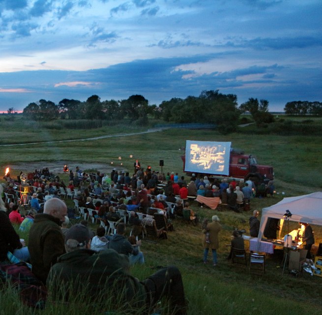 Freiluftkino in malerischer Landschaft: Zahlreiche Besucher genießen eine Filmvorführung unter freiem Himmel., © Tobias Rank