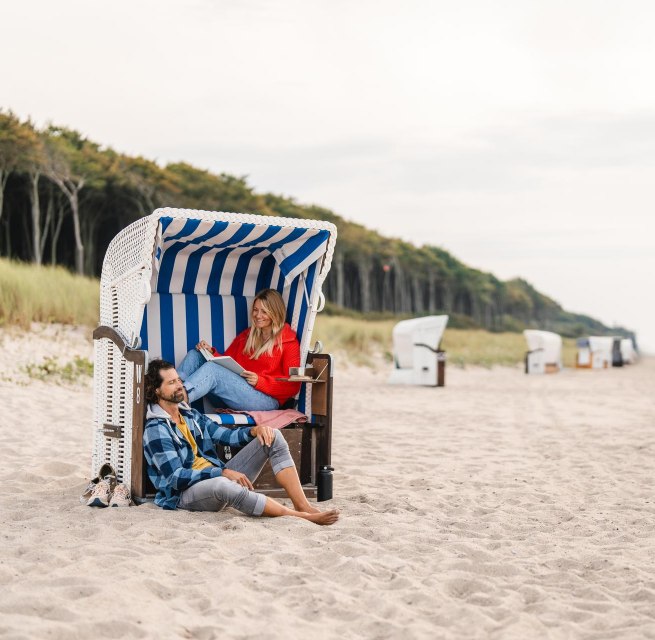 Pärchen sitzt in einem Strandkorb am Strand von Graal-Müritz an der Ostseeküste. Im Hintergrund ist der Küstenwald zu sehen.