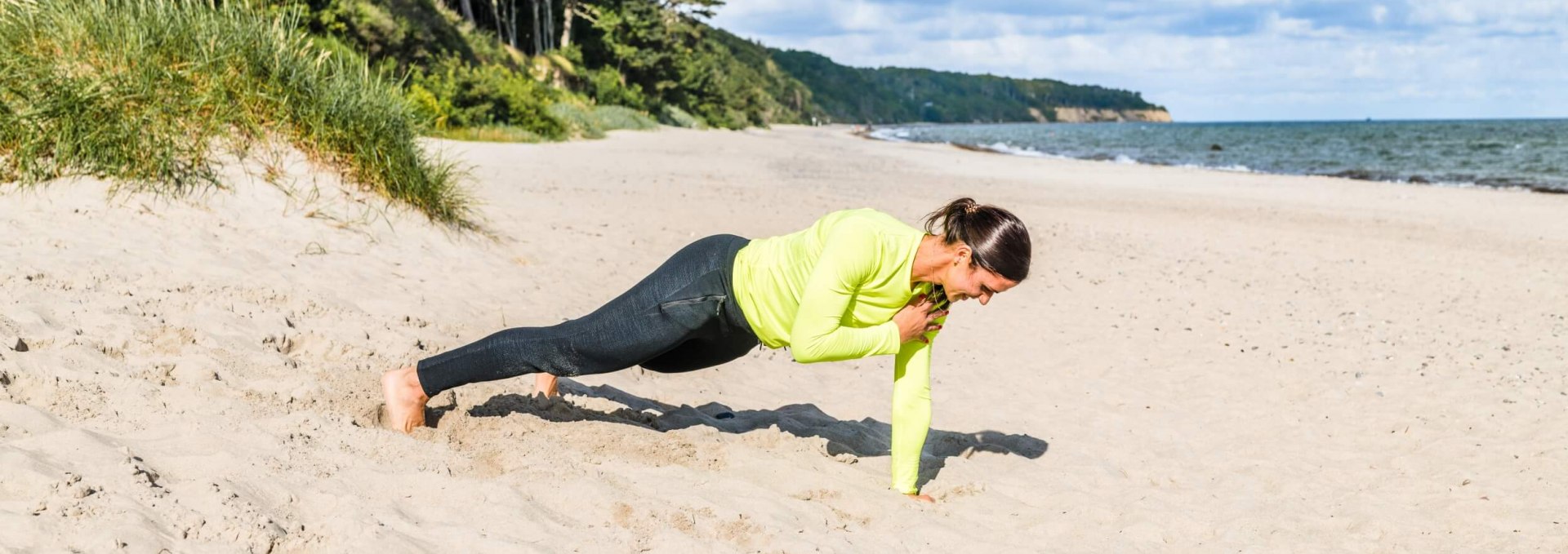 Stütz dich auf die Handflächen. Wenn du einen stabilen Stand hast, hebst du die linke Hand vom Boden ab und führst sie zur rechten Schulter. Einmal antippen und dann zurück auf den Strandsand. Achte darauf, dass Hüften und Körper nicht zur Seite schwingen, wenn du dir auf die Schultern tippst. Es soll sich ausschließlich die Hand zur gegenüberliegenden Schulter bewegen. 6-10 Wiederholungen pro Seite, © TMV/Tiemann