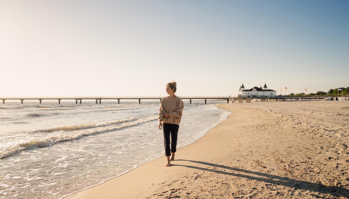 Frau spaziert am Strand von Ahlbeck zum Sonnenaufgang mit Seebrücke im Hintergrund