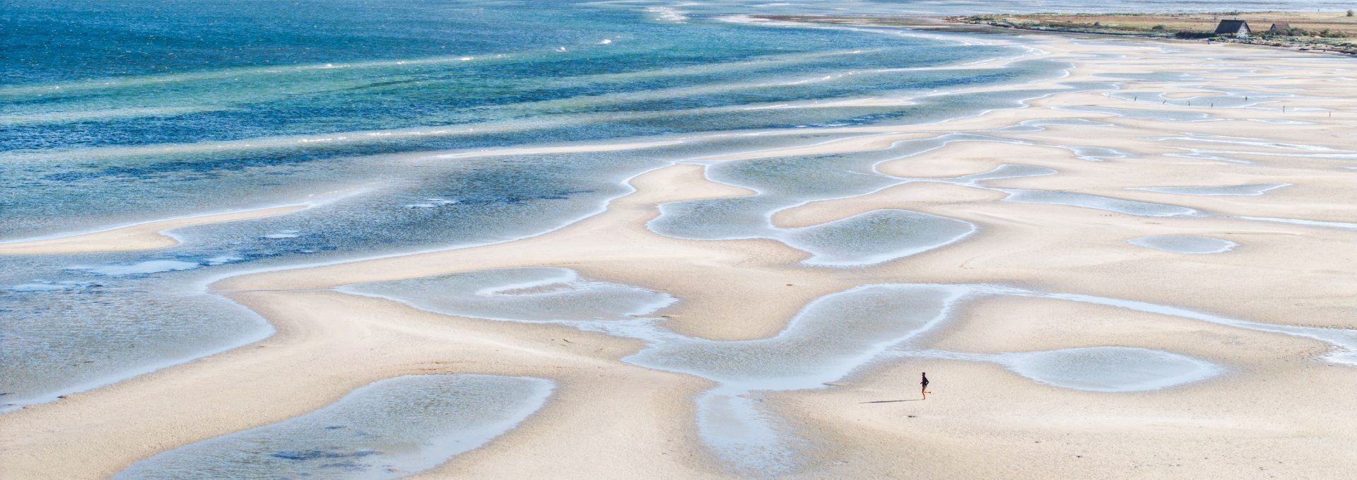 Weitläufige Sandbänke und flache Wasserflächen bei Gollwitz auf der Insel Poel, aufgenommen bei Ebbe unter klarem Himmel.