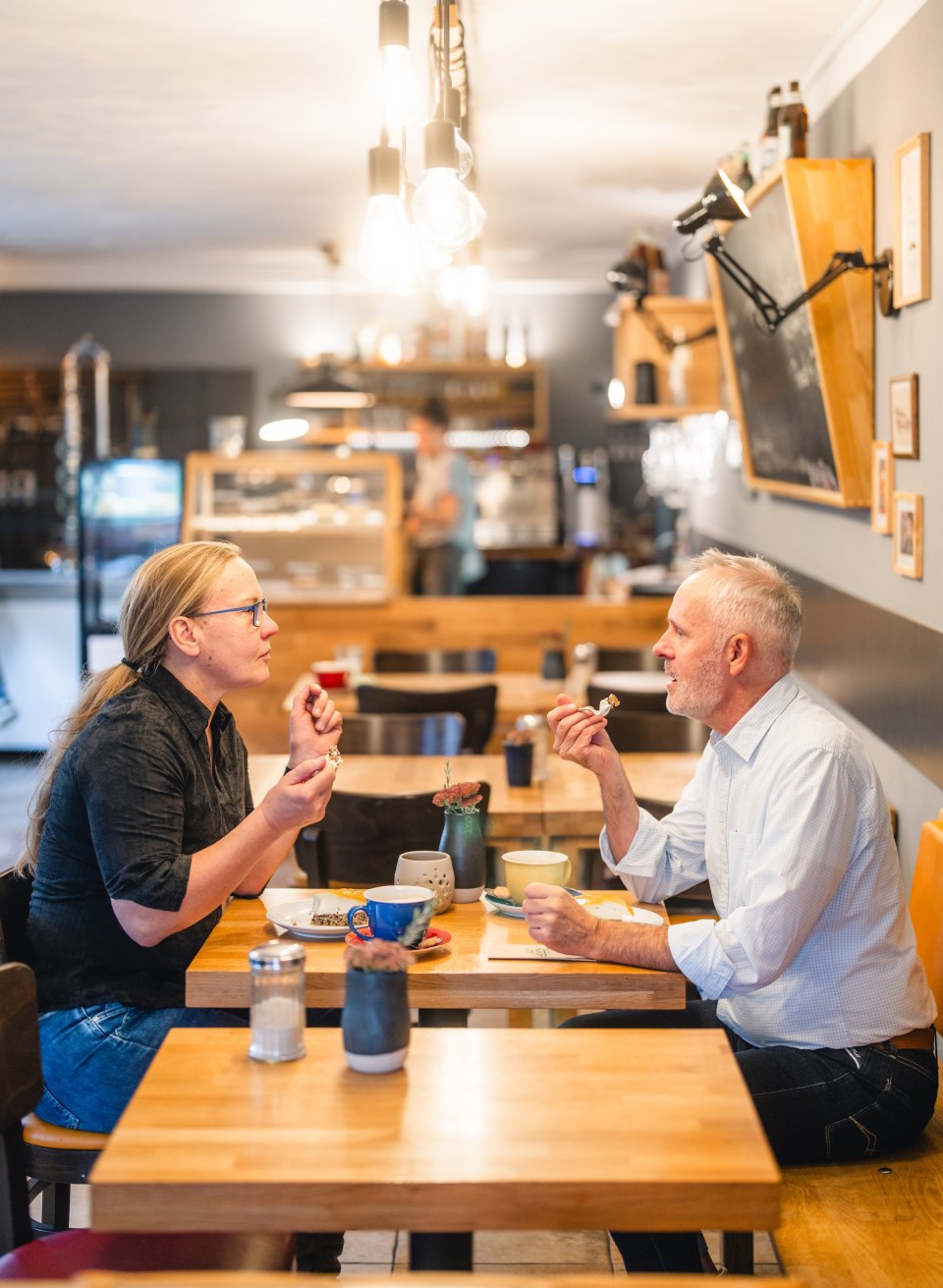 Zwei Personen genießen Kaffee und Kuchen in einem gemütlichen Café mit moderner Einrichtung.