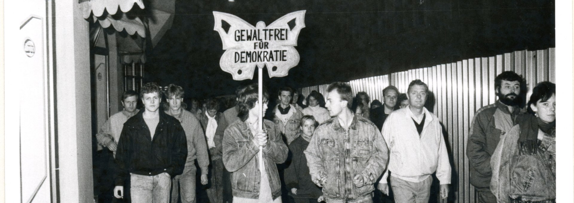 Demonstrierende führen ein Transparent in Form eines Schmetterlings mit sich, auf dem steht "Gewaltfrei für Demokratie", © Bundesarchiv/Stasi-Unterlagen-Archiv