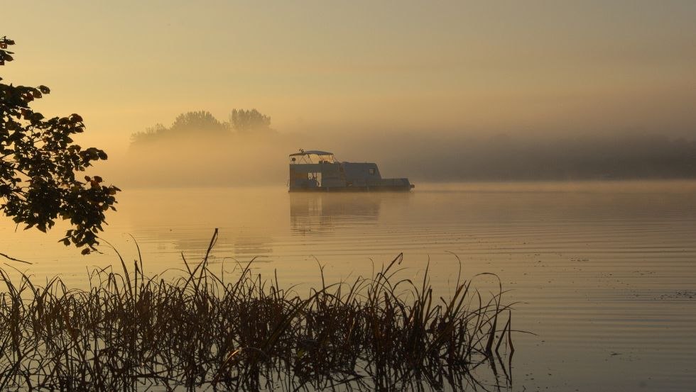 Sonnenaufgang auf dem See: mittendrin ein schwimmender Wohnwagen, © freecamper