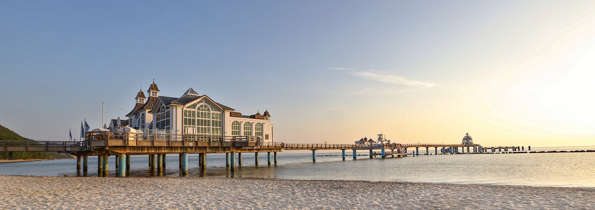 Die Seebrücke im Ostseebad Sellin bei Sonnenaufgang, mit feinem Sandstrand im Vordergrund und ruhiger Ostsee im Hintergrund.