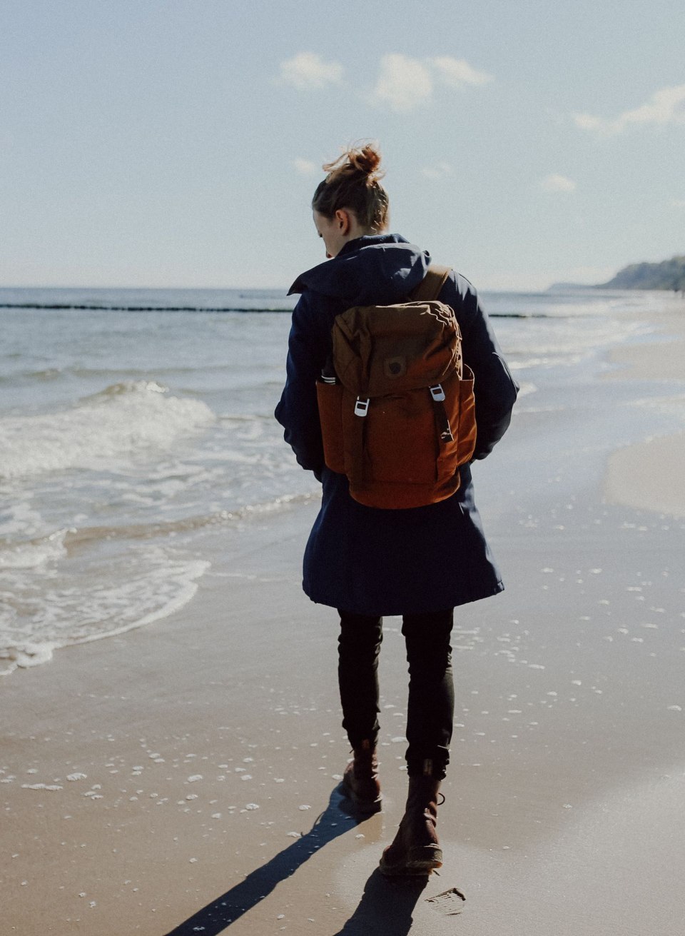 Eine Spaziergängerin wandert entlang der Küste der Insel Usedom, während die sanften Wellen den Strand umspülen. Mit einem Rucksack ausgestattet, begibt sie sich auf die Suche nach verborgenen Schätzen wie Bernsteinen, die hier oft an den Ufern zu finden sind.