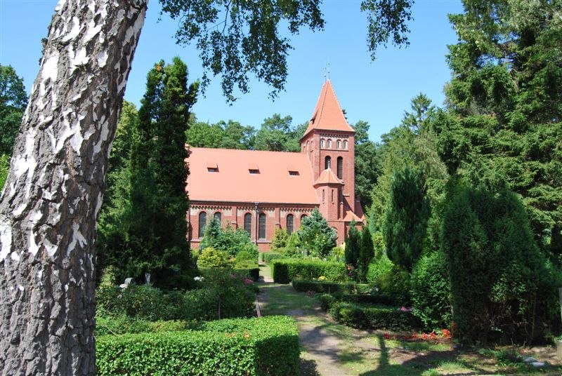 Die St.-Lukas-Kirche in Graal-Müritz, eine rote Backsteinkirche mit Turm, umgeben von grüner Gartenanlage und hohen Bäumen.