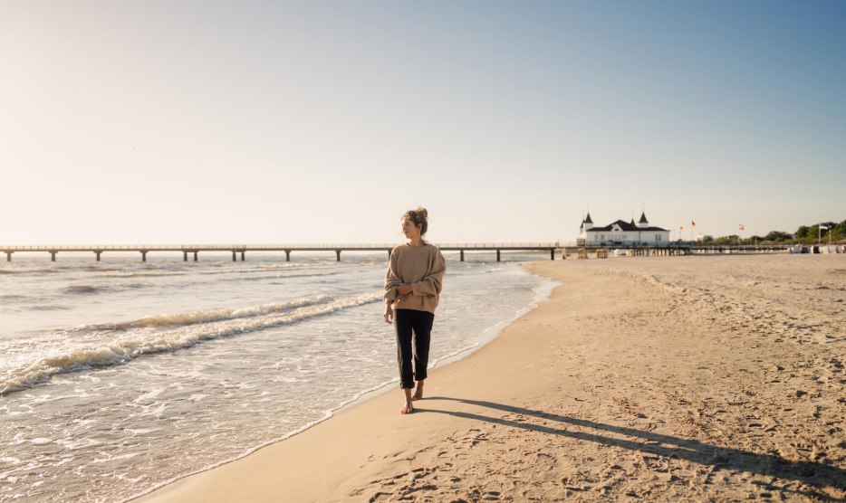 Frau spaziert am Strand von Ahlbeck zum Sonnenaufgang mit Seebrücke im Hintergrund