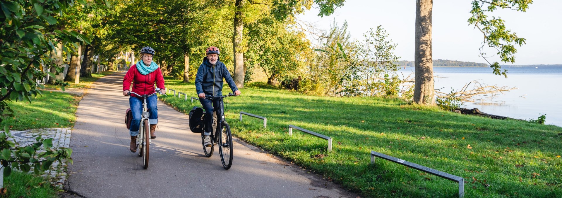 Zwei Radfahrer auf einem baumgesäumten Weg am Ufer des Schweriner Sees, umgeben von herbstlicher Natur.