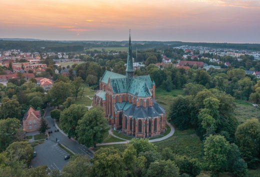 Luftaufnahme des Münsters in Bad Doberan bei Sonnenuntergang, umgeben von Bäumen, Wiesen und der umliegenden Stadt.