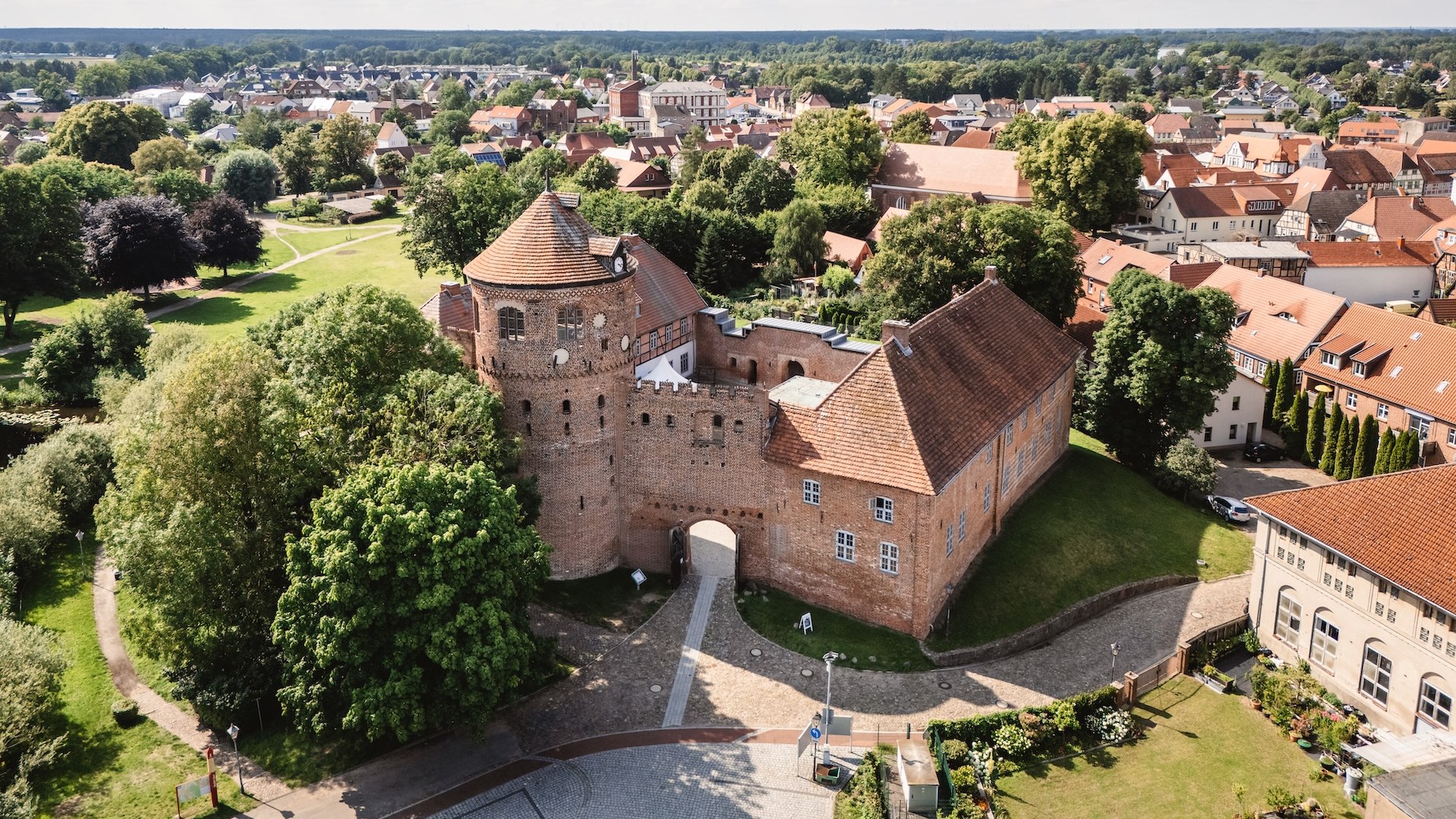 Eine Luftaufnahme der historischen Burg Neustadt-Glewe, umgeben von grünen Bäumen und der malerischen Altstadt mit roten Ziegeldächern.