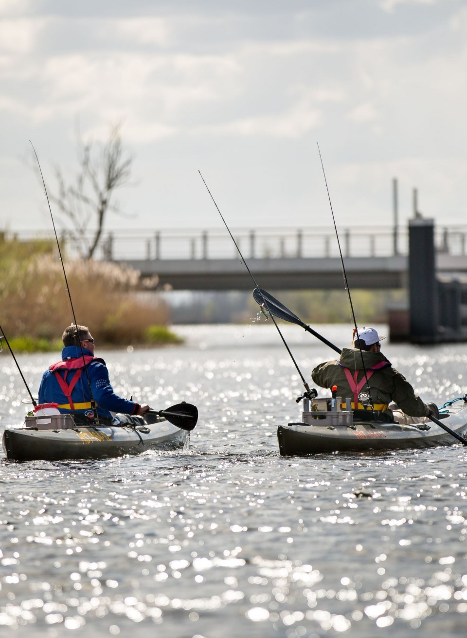 Zwei Angler paddeln in ihren Kajaks die Peene hinunter, während ihre Ruten bereit für den nächsten Fang sind. Die friedliche Atmosphäre auf dem Wasser und das Glitzern der Sonnenstrahlen schaffen eine perfekte Kulisse für eine entspannte Angeltour.