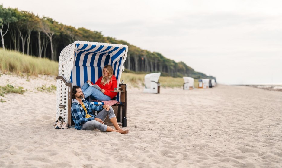 Pärchen sitzt in einem Strandkorb am Strand von Graal-Müritz an der Ostseeküste. Im Hintergrund ist der Küstenwald zu sehen.