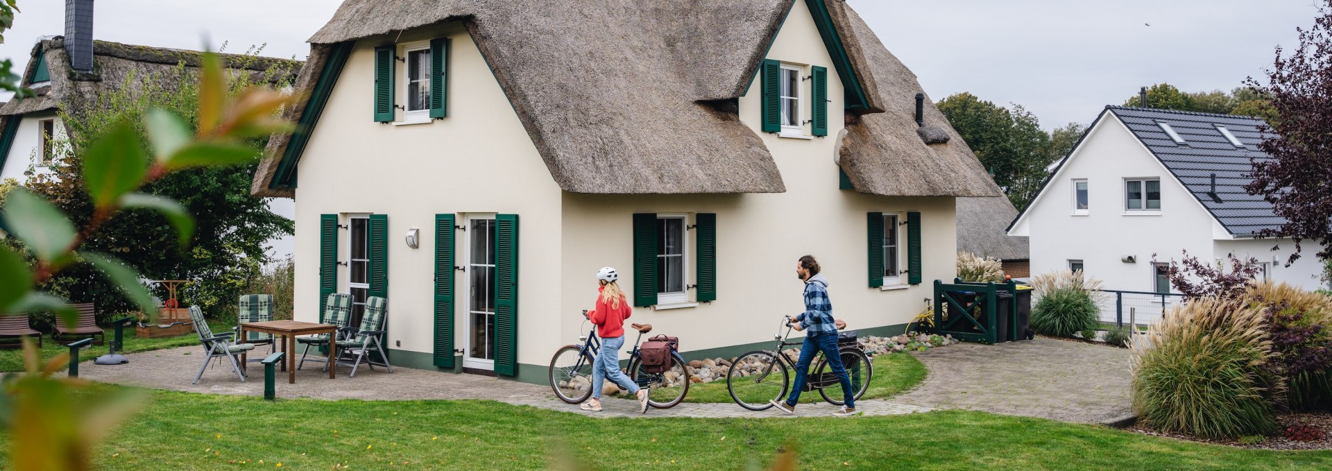 Ein Paar mit Fahrrädern vor einem charmanten Reetdach-Ferienhaus auf der Insel Poel.