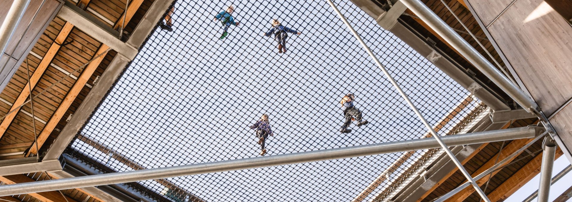 Blick von unten durch ein großes Sicherheitsnetz in einem Holzturm, auf dem mehrere Kinder stehen und spielen.